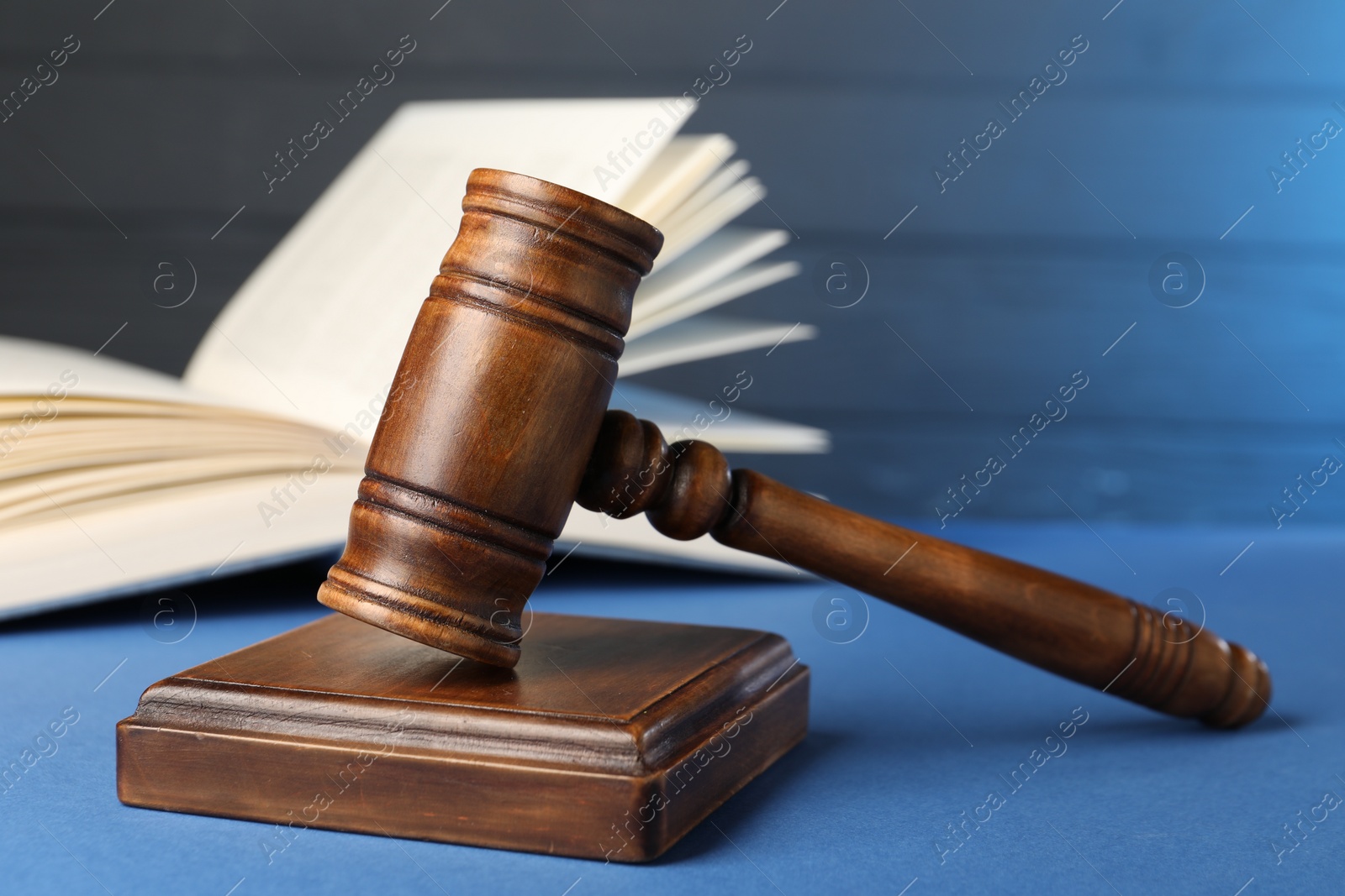 Photo of Wooden gavel, sound block and book on blue table, closeup