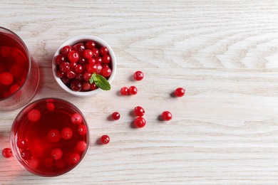 Photo of Tasty cranberry juice in glasses and fresh berries on white wooden table, flat lay. Space for text