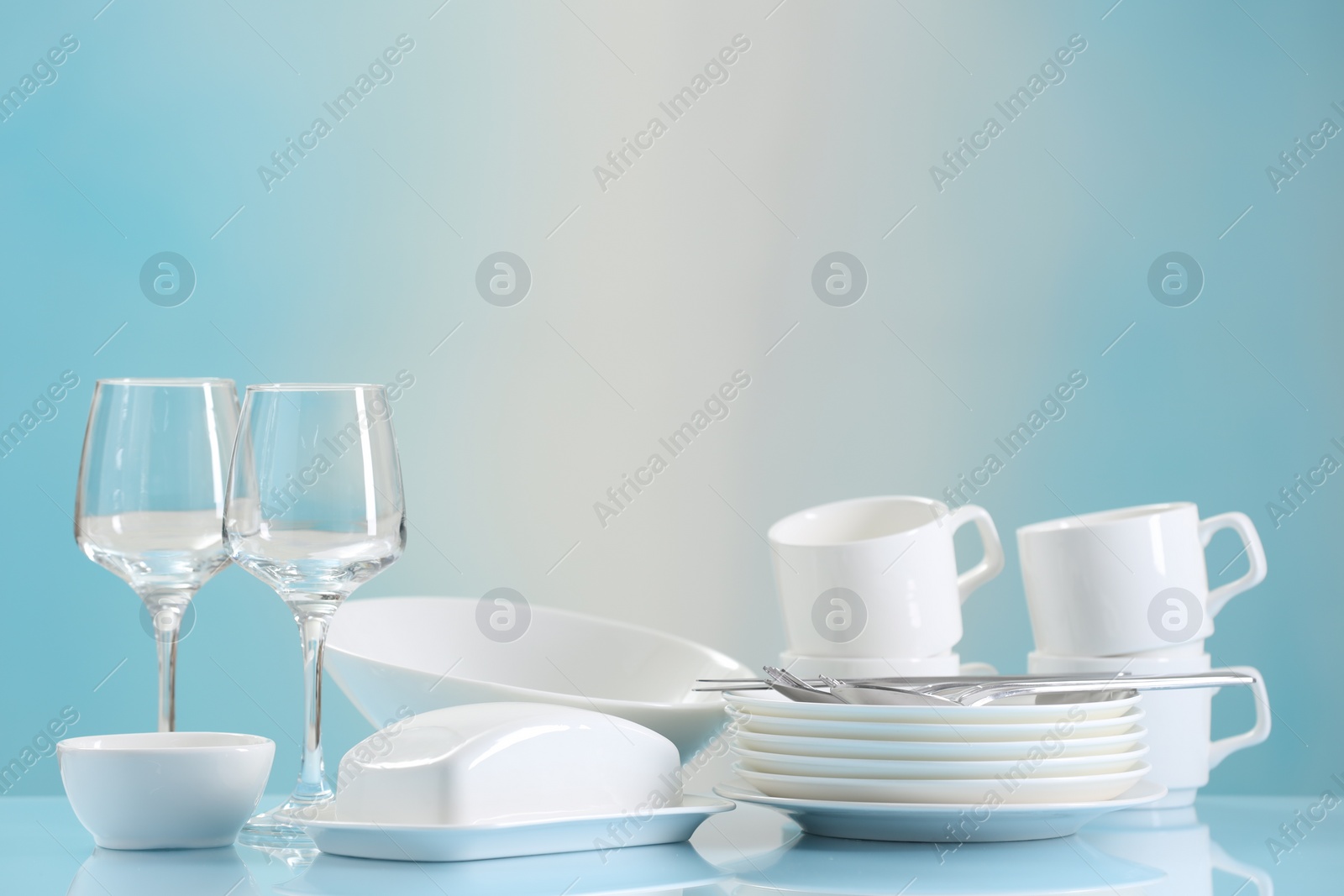 Photo of Set of many clean dishware, cutlery and glasses on light blue table