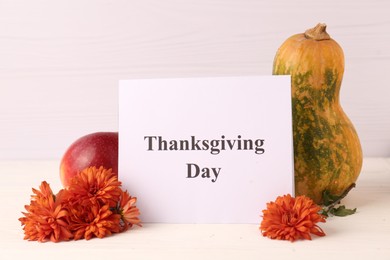 Photo of Thanksgiving day, holiday celebrated every fourth Thursday in November. Card, apple, pumpkin and chrysanthemum flowers on white wooden table