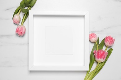 Photo of Empty photo frame and beautiful flowers on white marble background, flat lay. Space for design