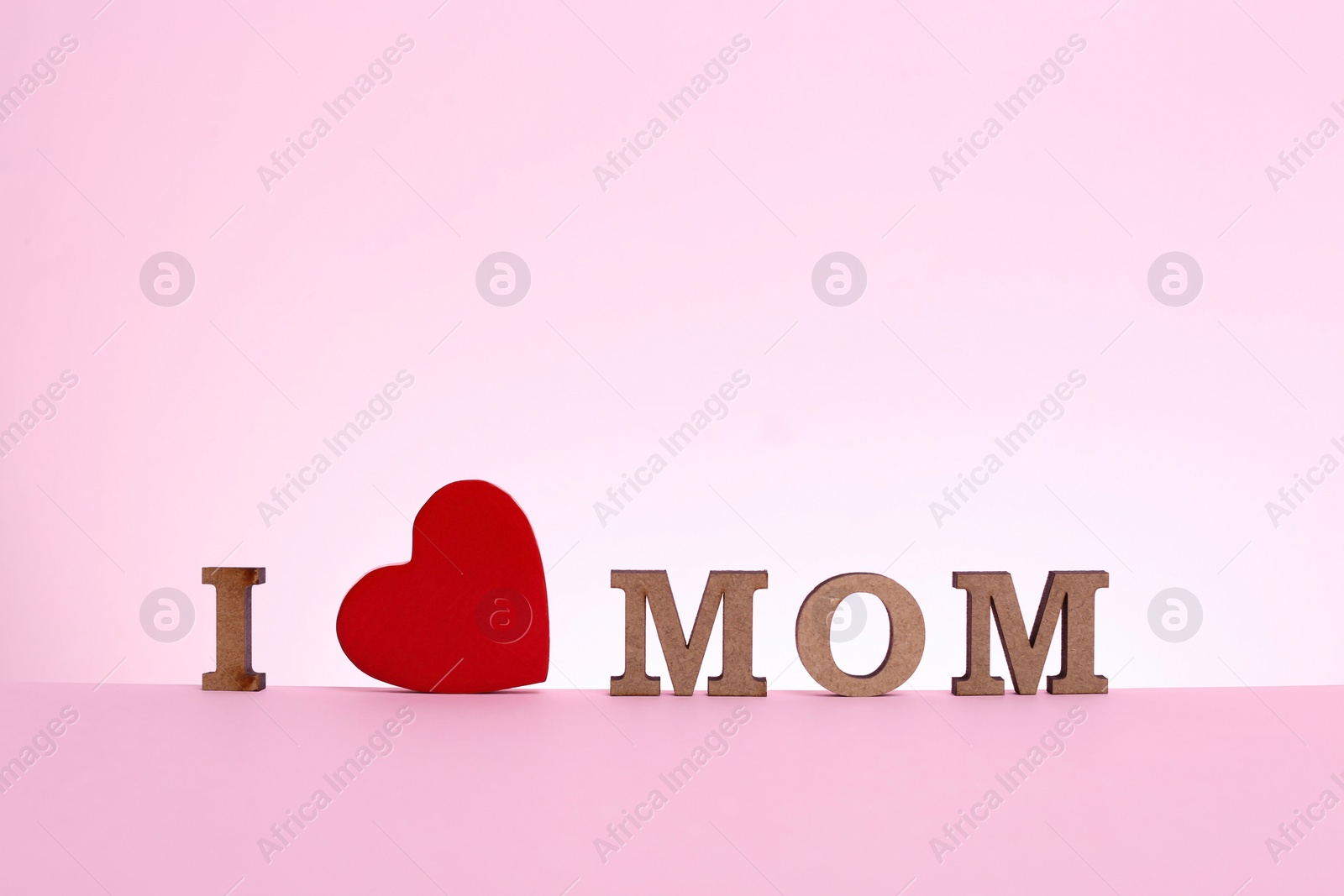 Photo of Phrase I LOVE MOM made of wooden letters and red heart for Mother's Day on color background