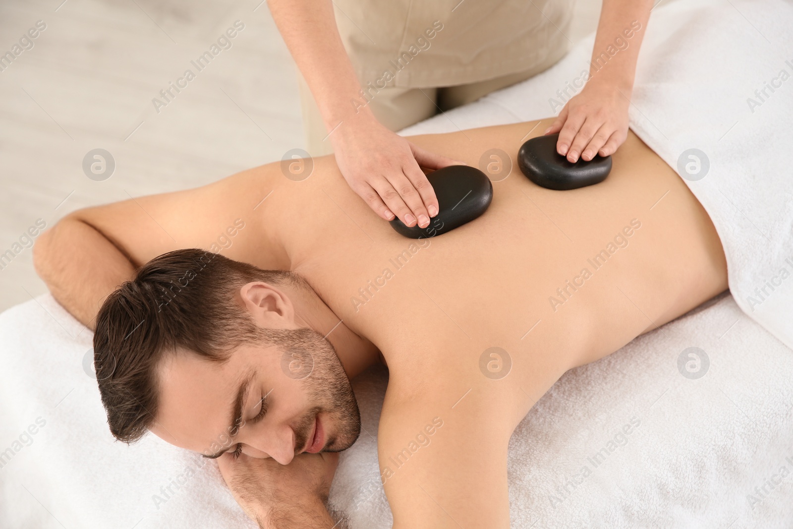 Photo of Handsome man receiving hot stone massage in spa salon, above view