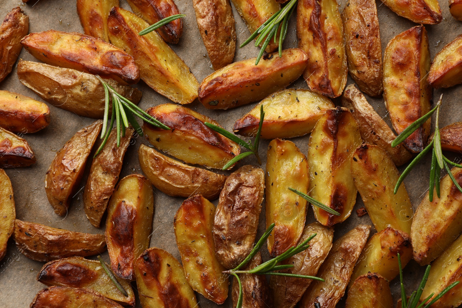 Photo of Tasty baked potato and aromatic rosemary on parchment paper, flat lay