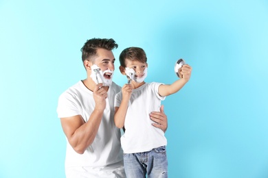 Father and son shaving on color background