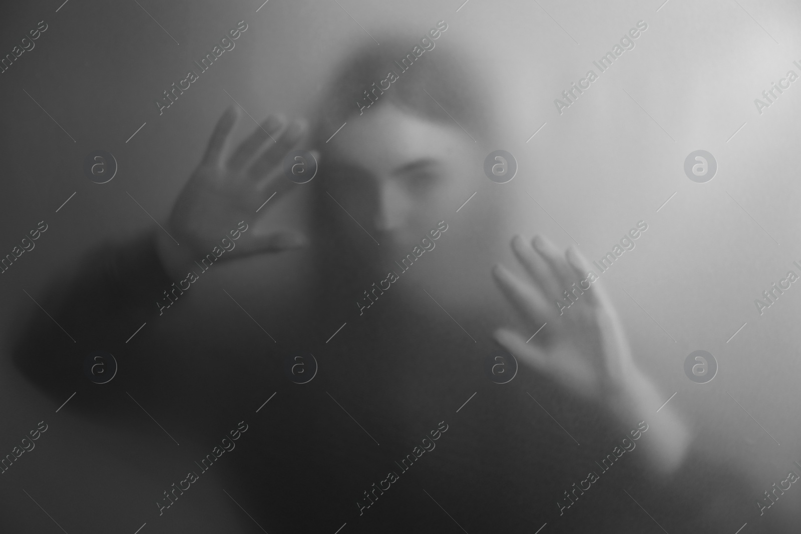 Photo of Silhouette of ghost behind fabric against light grey background. Black and white effect