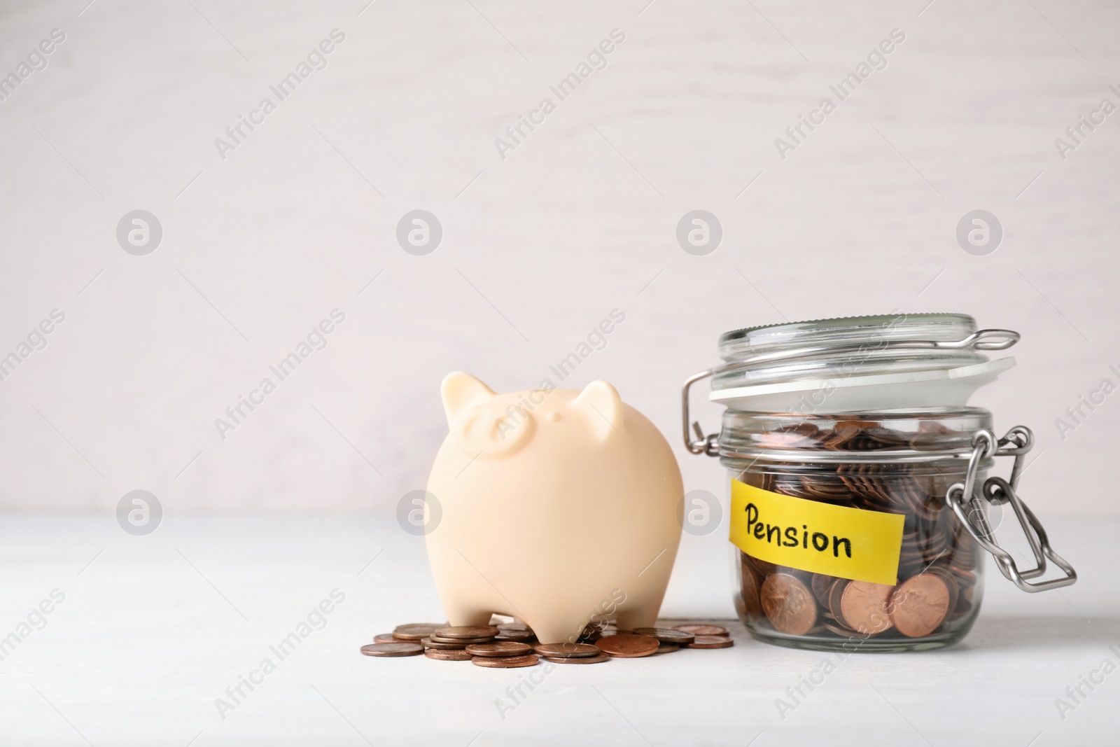 Photo of Piggy bank and jar of coins with word PENSION on table. Space for text