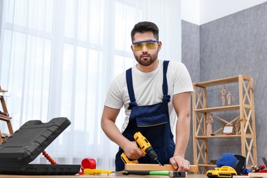 Photo of Young worker using electric drill at table in workshop