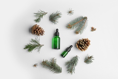 Flat lay composition with bottles of essential oils and pine branches on white background