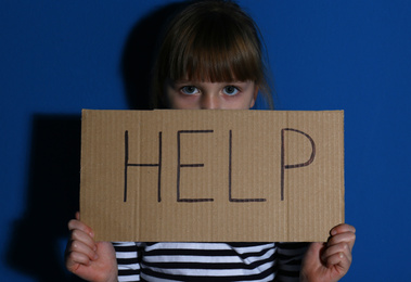 Abused little girl with sign HELP near blue wall. Domestic violence concept