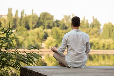 Photo of Man meditating on wooden pier near river, back view. Space for text