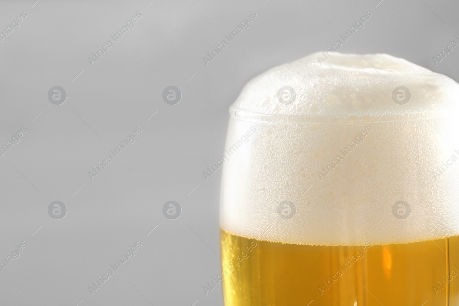 Photo of Glass of tasty beer with foam on light background, closeup