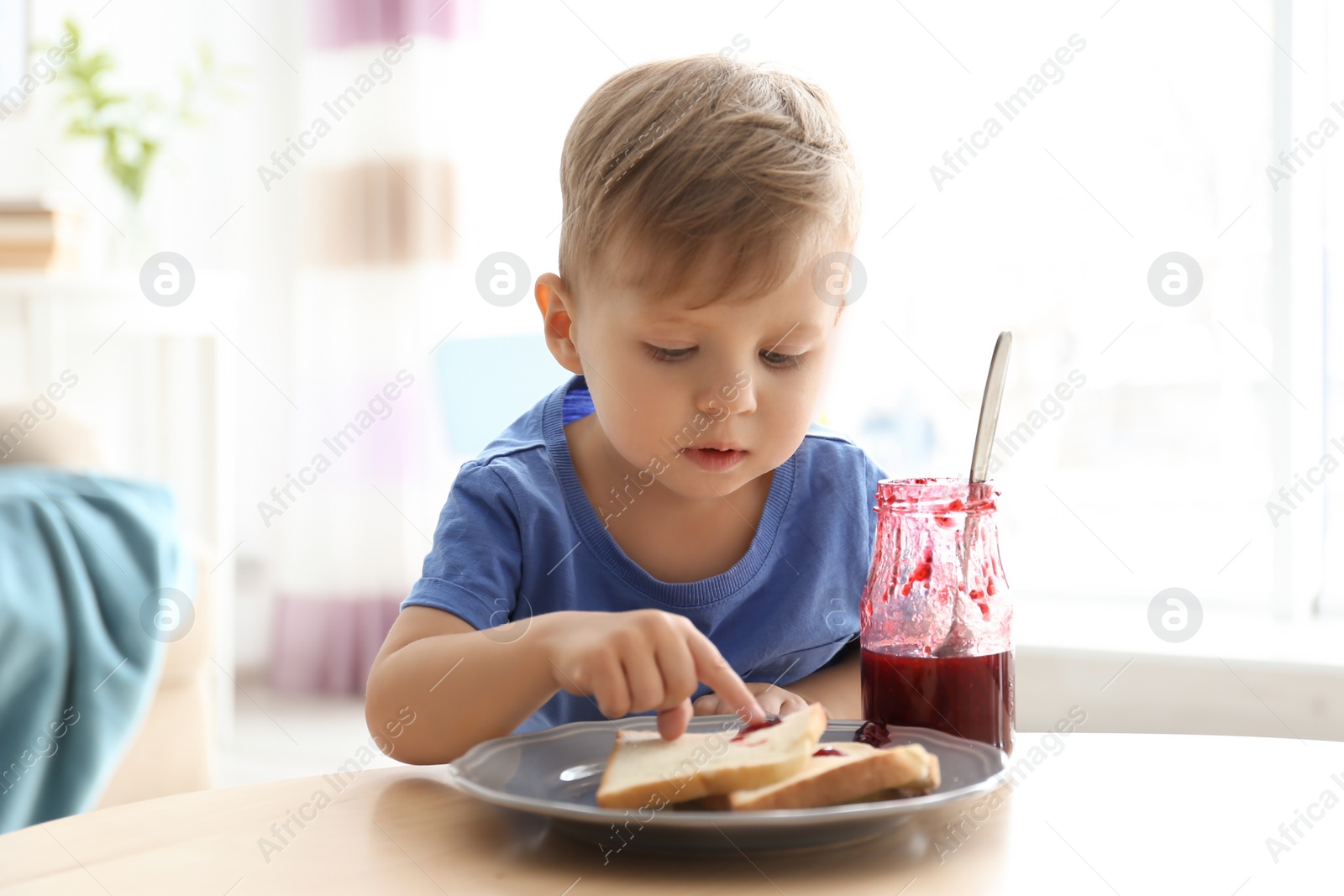 Photo of Little boy having breakfast with toast bread and jam at table in living room