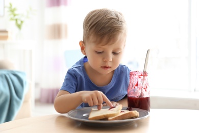 Little boy having breakfast with toast bread and jam at table in living room