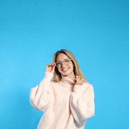 Beautiful young woman wearing knitted sweater on light blue background