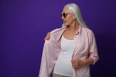 Portrait of beautiful mature woman on violet background, space for text