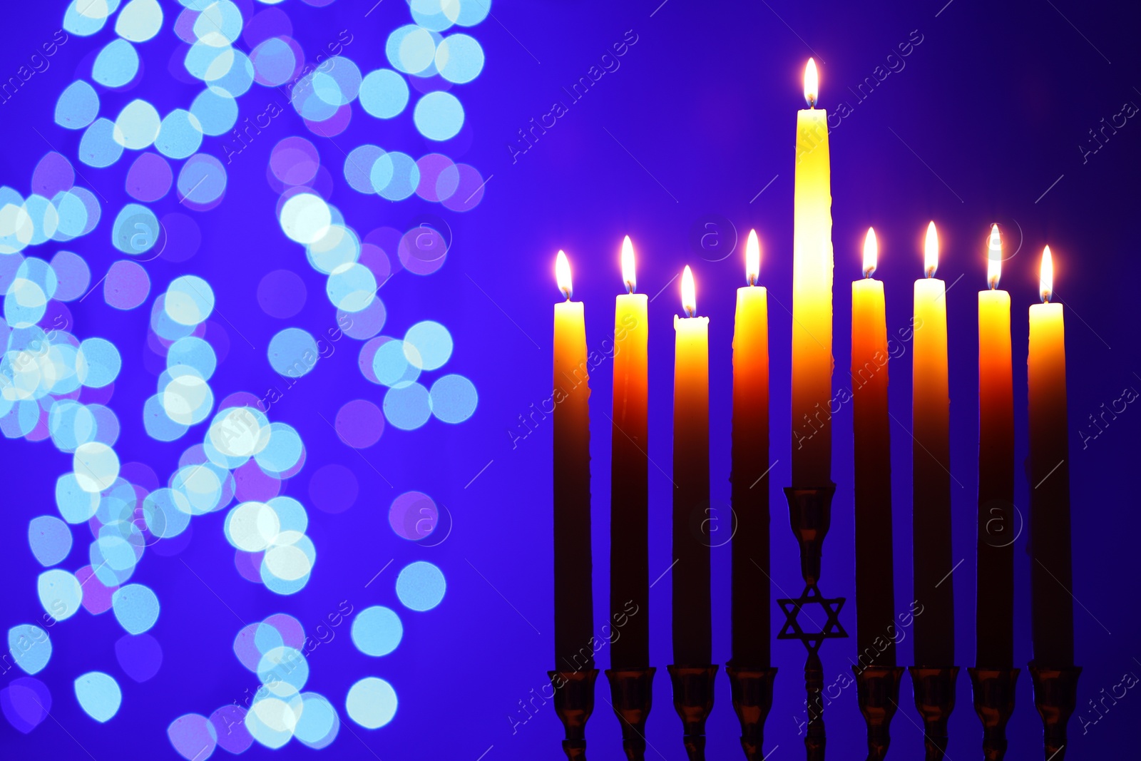 Photo of Hanukkah celebration. Menorah with burning candles on blue background with blurred lights, space for text