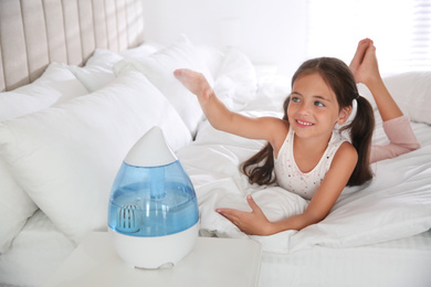 Photo of Cute little girl in bedroom with modern air humidifier