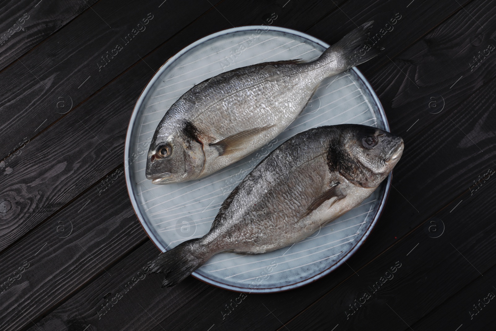 Photo of Fresh raw dorado fish on black wooden table, top view