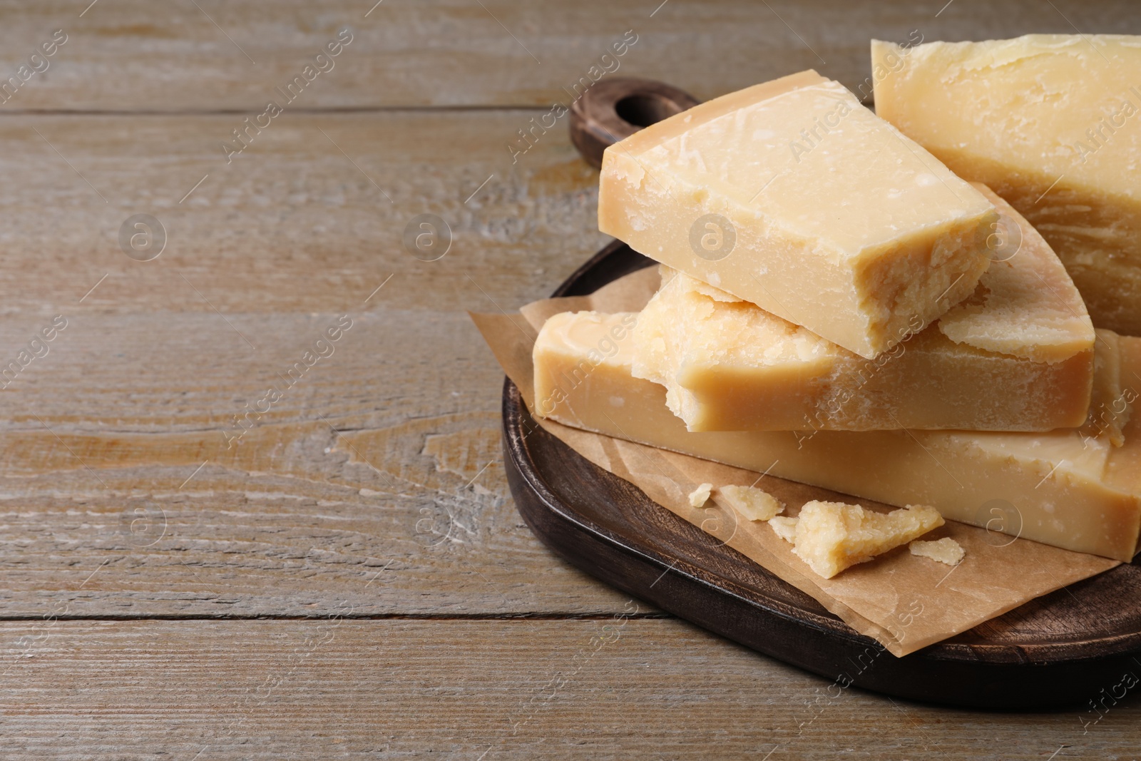 Photo of Pieces of delicious parmesan cheese on wooden table. Space for text