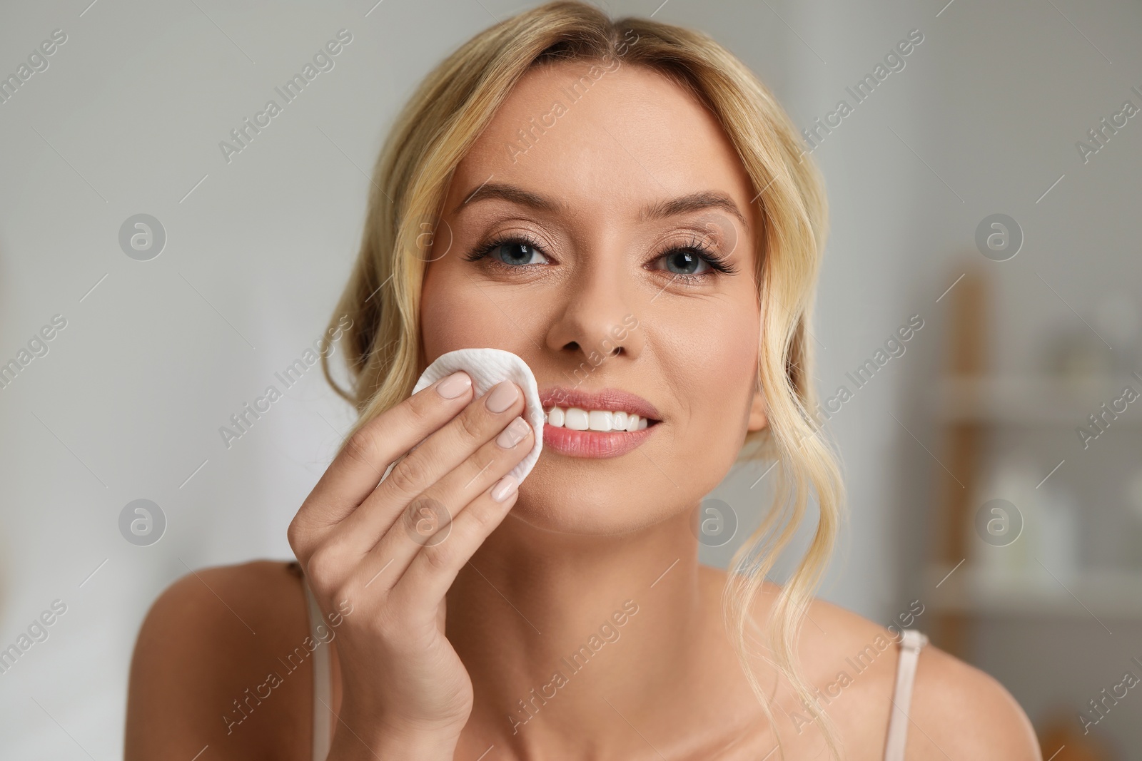 Photo of Smiling woman removing makeup with cotton pad indoors, closeup