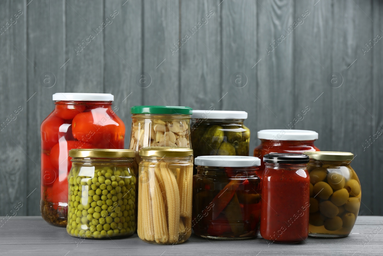 Photo of Glass jars with different pickled vegetables on grey wooden background
