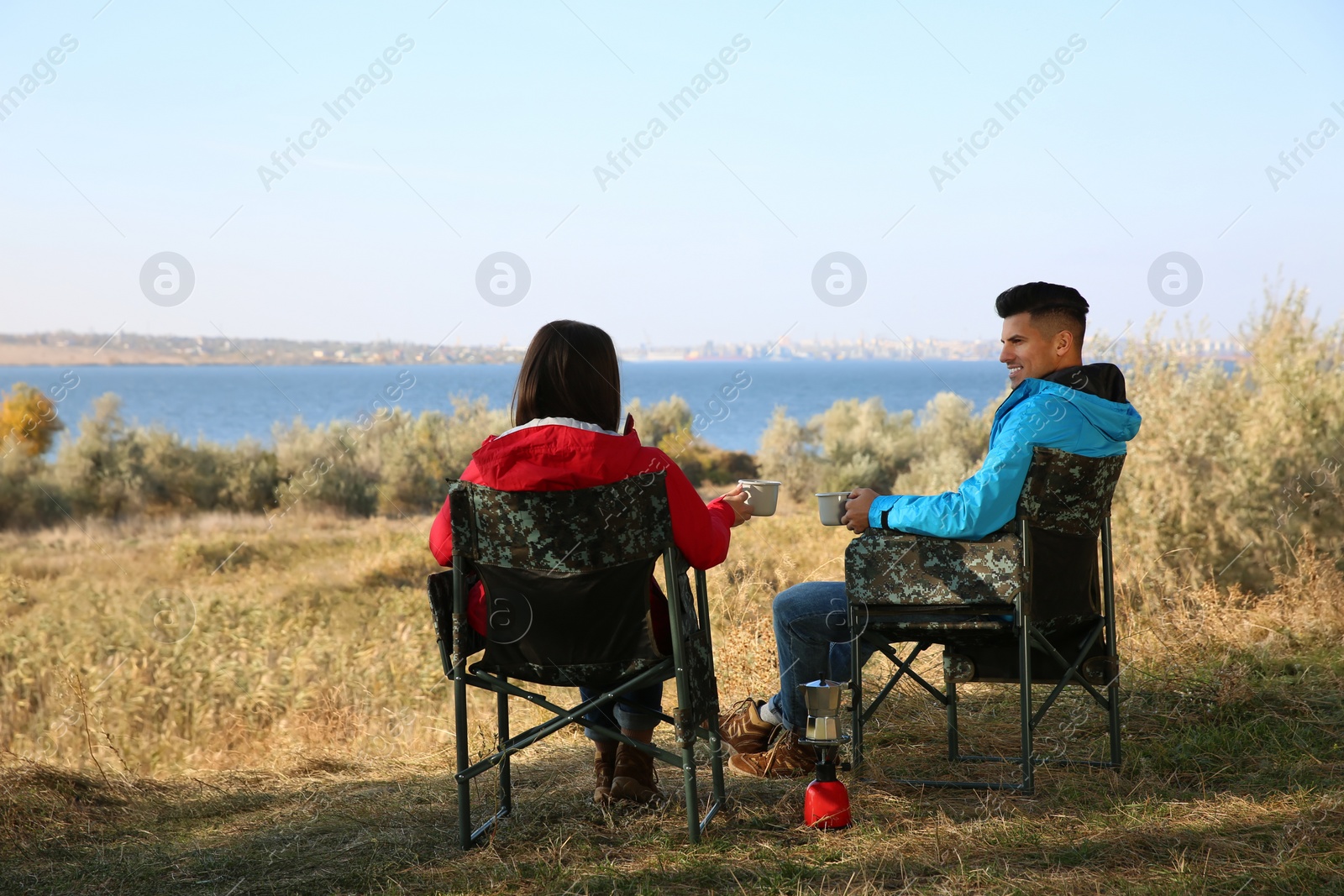 Photo of Couple resting in camping chairs and enjoying hot drink outdoors