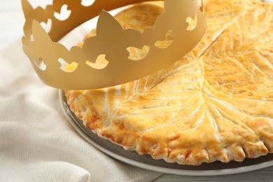 Photo of Traditional galette des Rois with paper crown on table, closeup