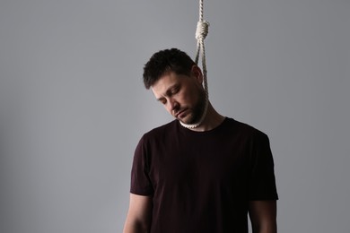 Depressed man with rope noose on neck against light grey background