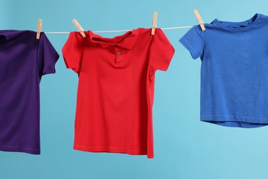 Photo of Many colorful t-shirts drying on washing line against light blue background