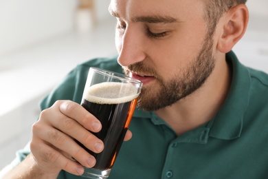 Photo of Handsome man with cold kvass indoors, closeup. Traditional Russian summer drink