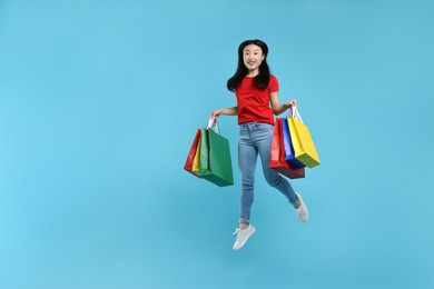 Happy woman jumping with shopping bags on light blue background