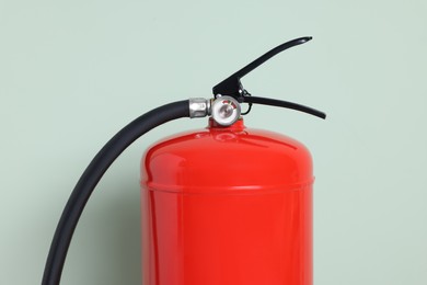 Photo of Red fire extinguisher against light green background, closeup