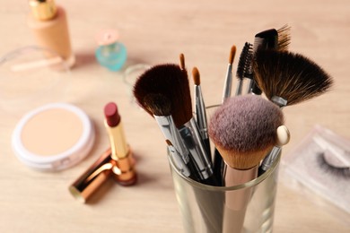 Photo of Set of professional brushes and makeup products on wooden table, closeup. Space for text