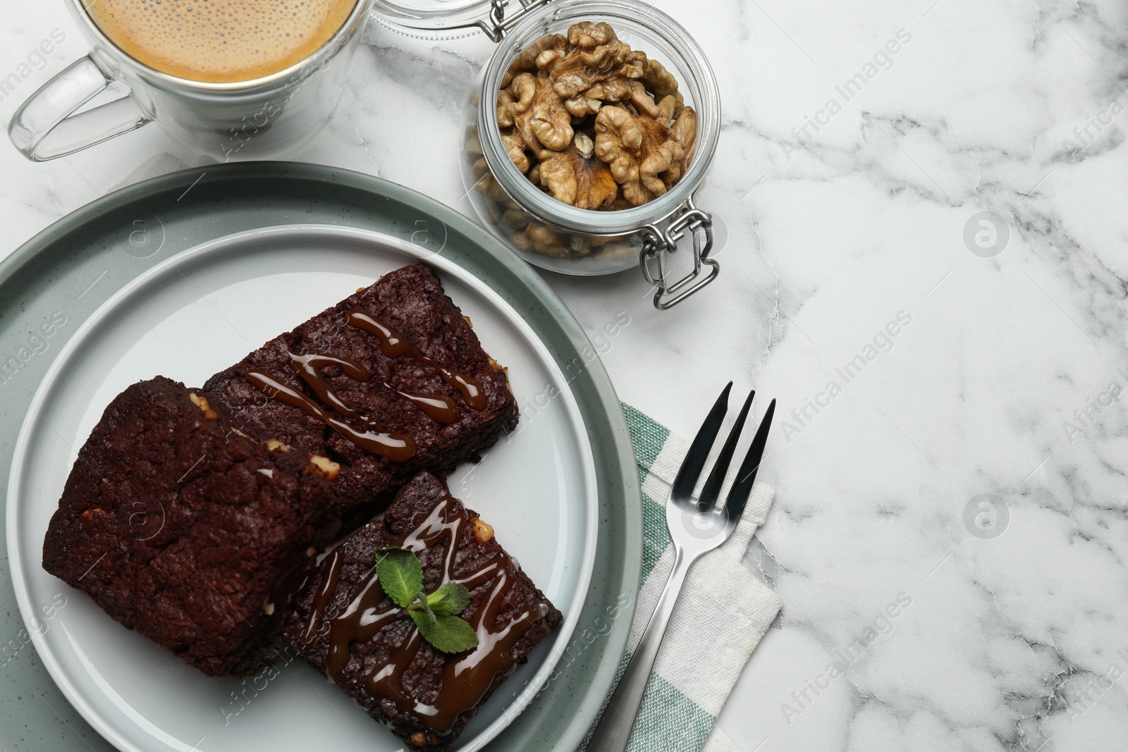 Photo of Delicious chocolate brownies with nuts, caramel sauce and coffee on white marble table, flat lay. Space for text