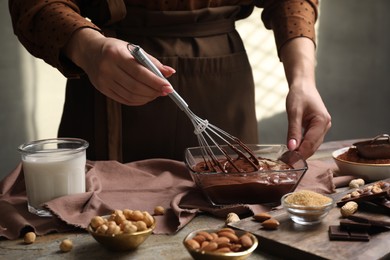 Photo of Woman mixing delicious chocolate cream with whisk at grey textured table, closeup