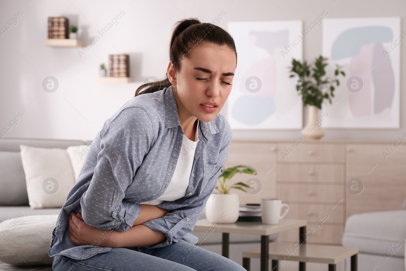 Photo of Young woman suffering from stomach ache at home. Food poisoning