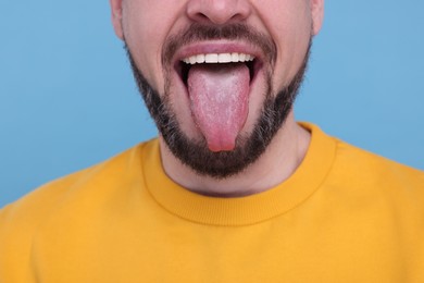 Happy man showing his tongue on light blue background, closeup