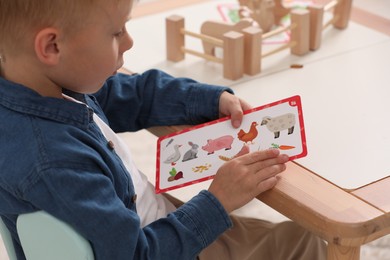 Little boy playing with set of wooden animals and fence at table indoors, closeup. Child's toy