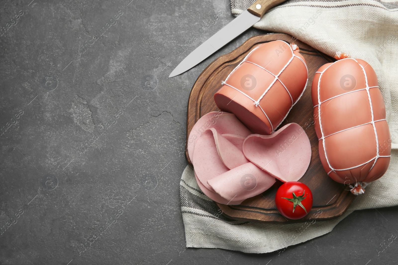 Photo of Board with tasty boiled sausages and tomato on grey textured table, flat lay. Space for text