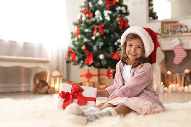 Photo of Cute little child in Santa hat with Christmas gift box at home