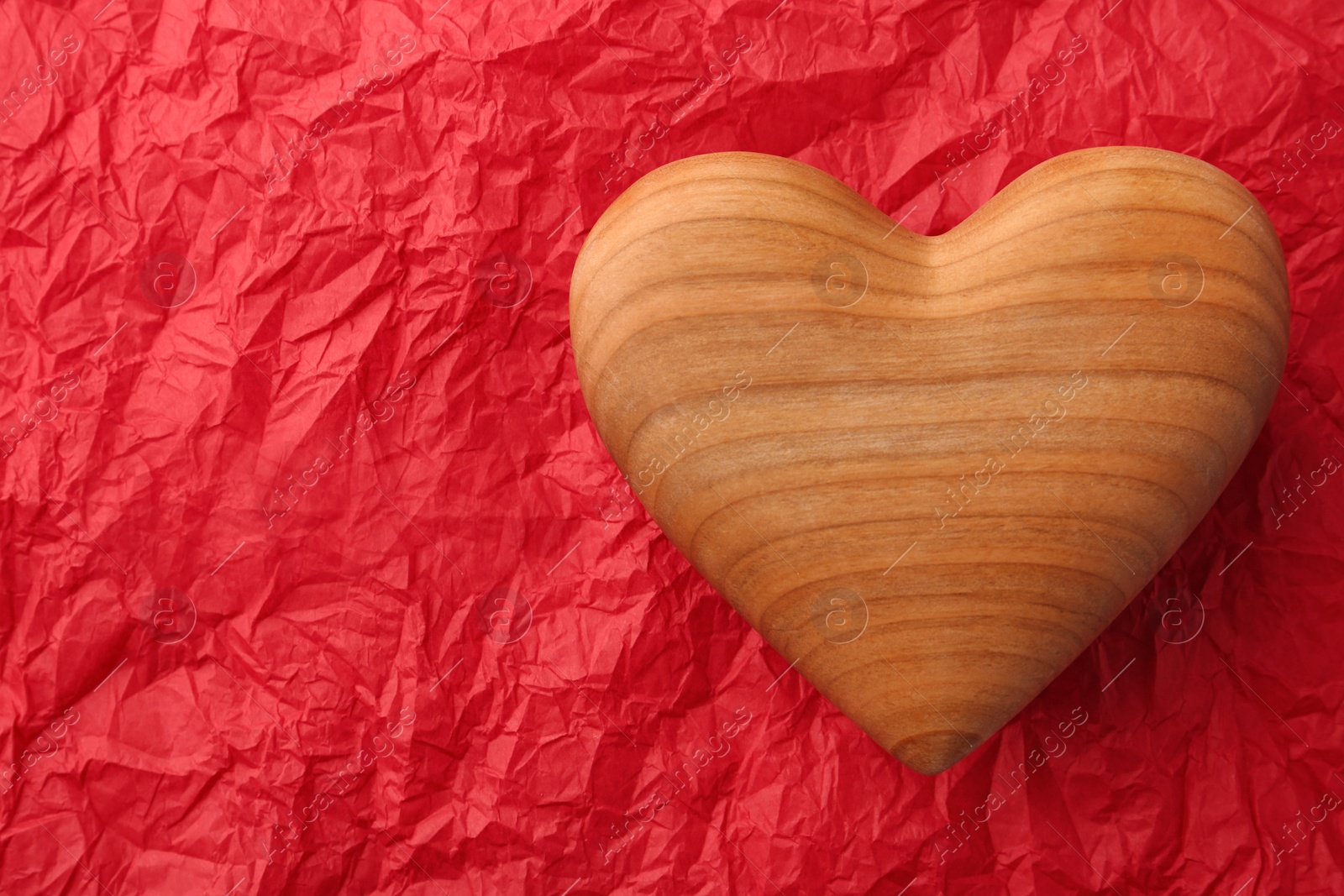 Photo of Wooden heart on red crumpled paper, top view. Space for text