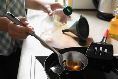 Photo of Woman with used cooking oil and empty bottle near stove in kitchen, closeup