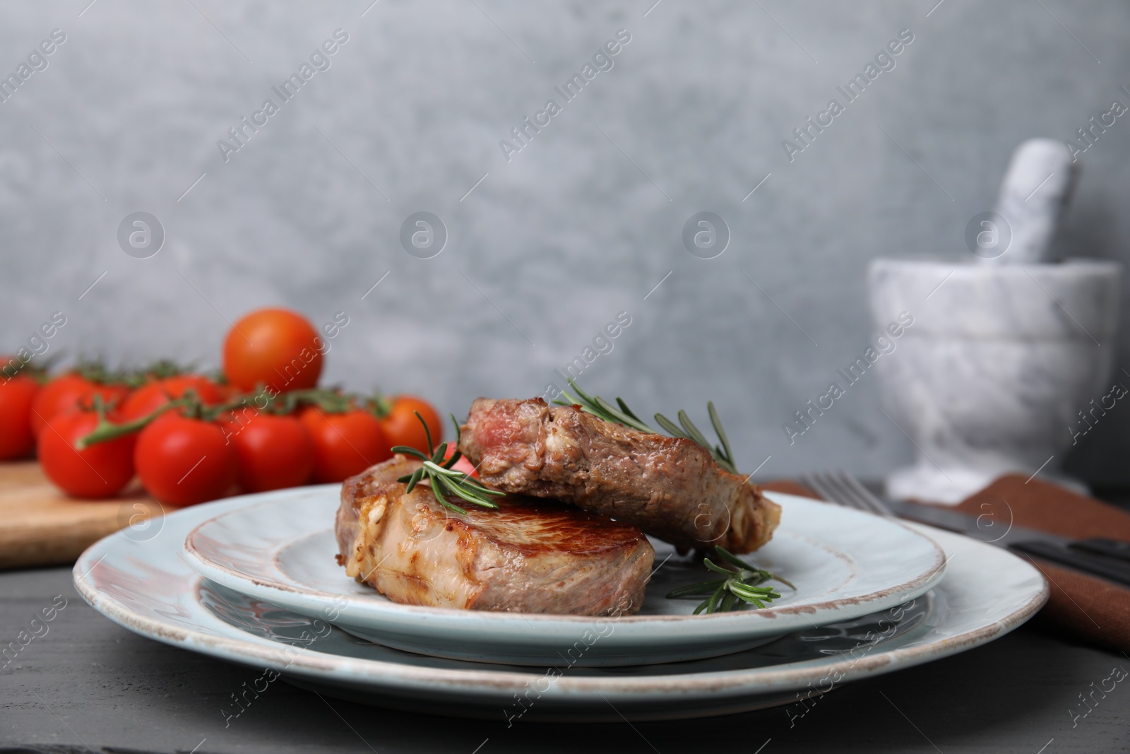 Photo of Delicious fried meat with rosemary on grey table, closeup