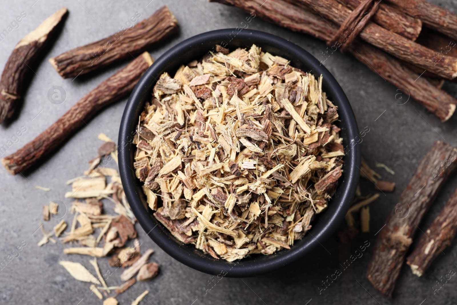 Photo of Dried sticks of liquorice root and shavings on grey table, flat lay