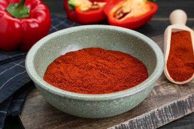 Photo of Bowl of aromatic paprika and fresh peppers on black wooden table