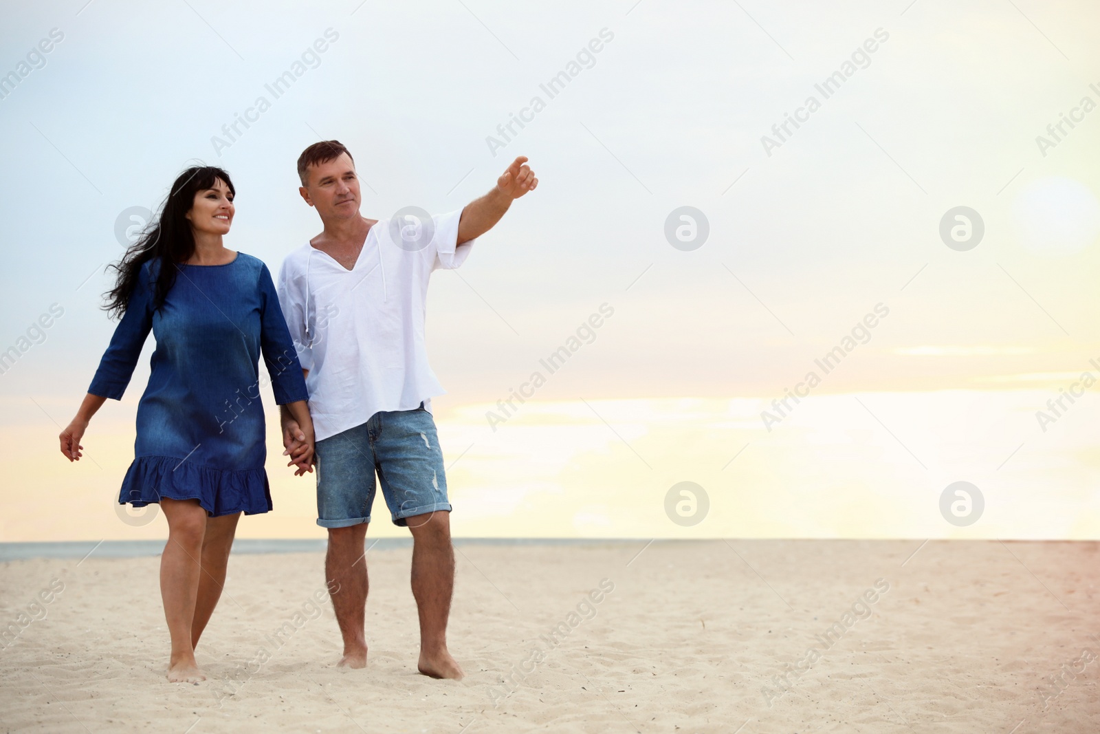 Photo of Happy mature couple walking together on sea beach at sunset. Space for text