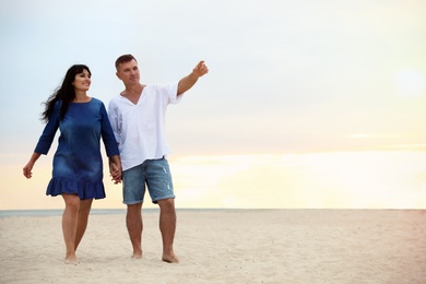 Photo of Happy mature couple walking together on sea beach at sunset. Space for text