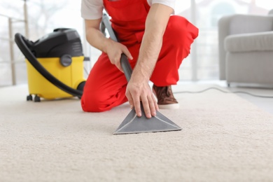 Male worker cleaning carpet with vacuum in living room