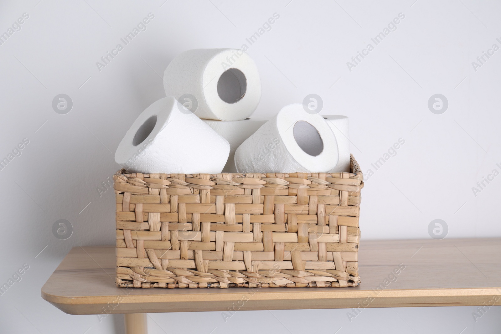 Photo of Toilet paper rolls in wicker basket on wooden table near white wall